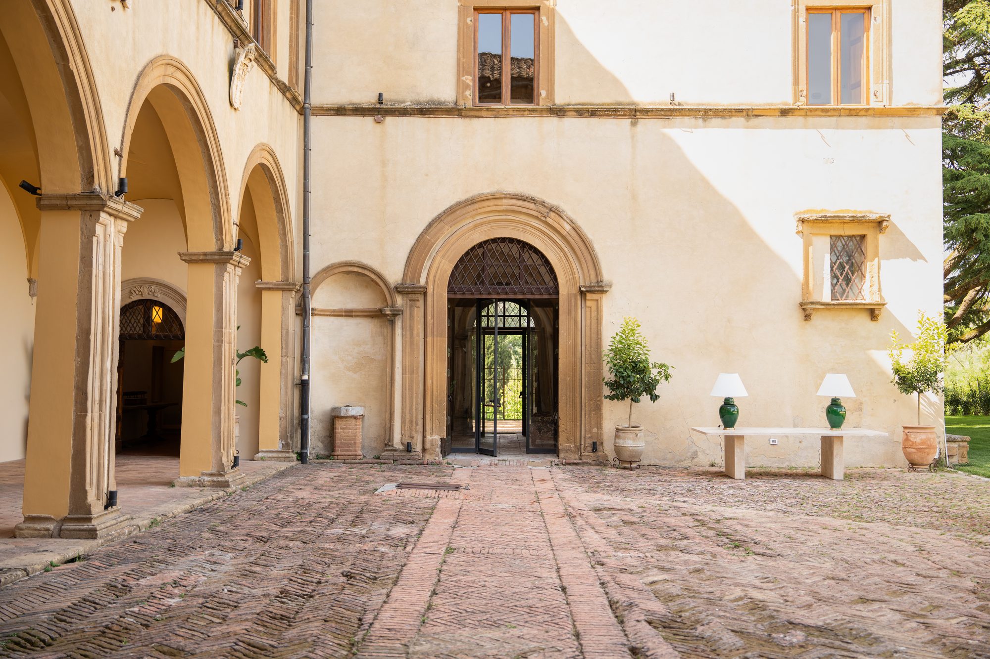Il cortile porticato di Volte Alte di giorno, con il pavimento a spina e il portone ad arco