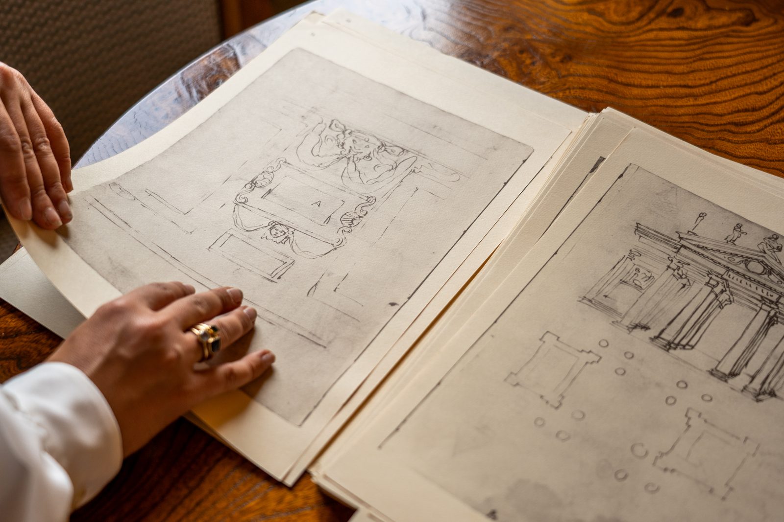 Due mani sfogliano disegni antichi della villa su un tavolo di legno