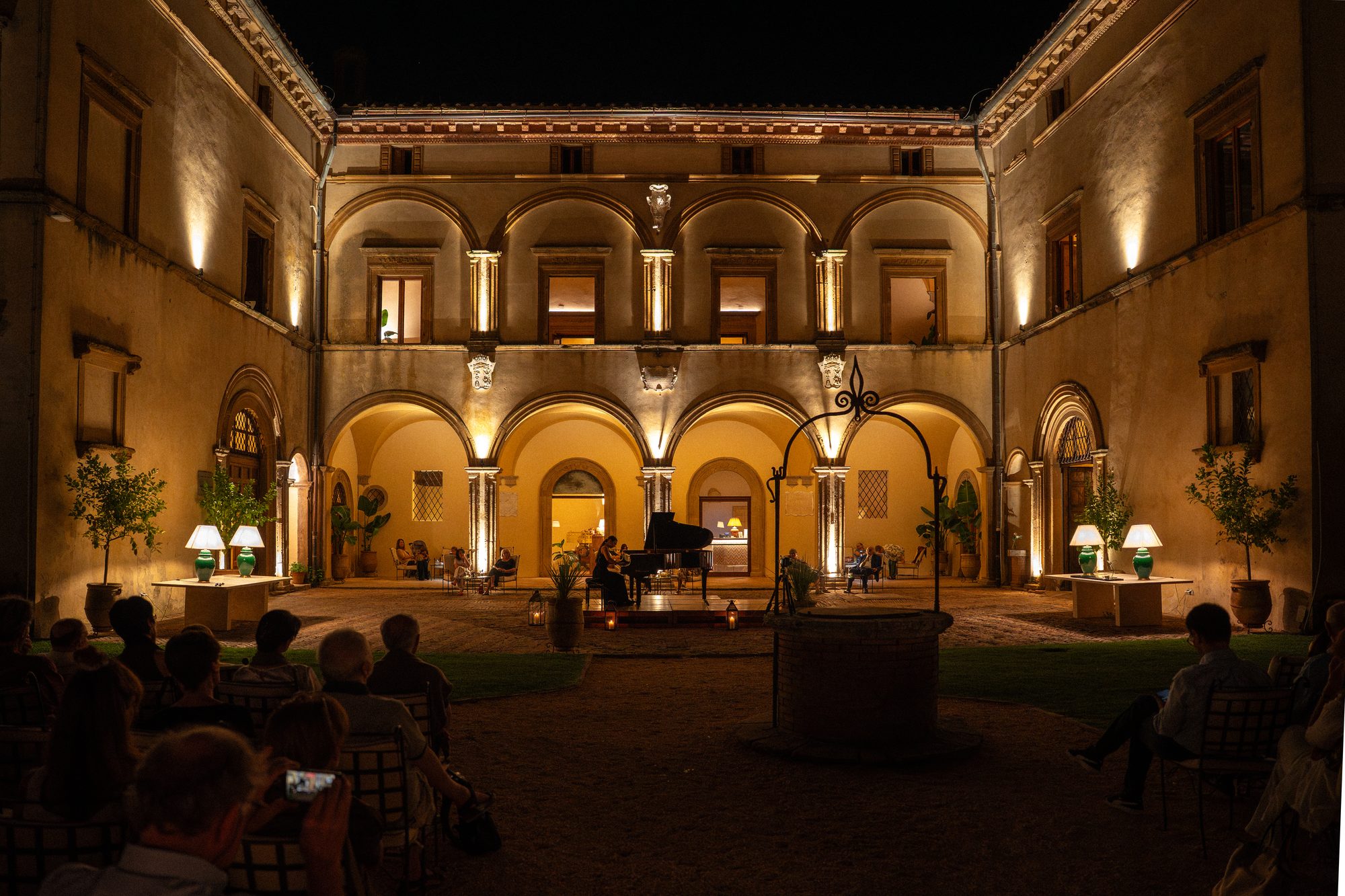 Il cortile di Volte Alte di sera, con il pozzo, il pianoforte e il pubblico di spalle