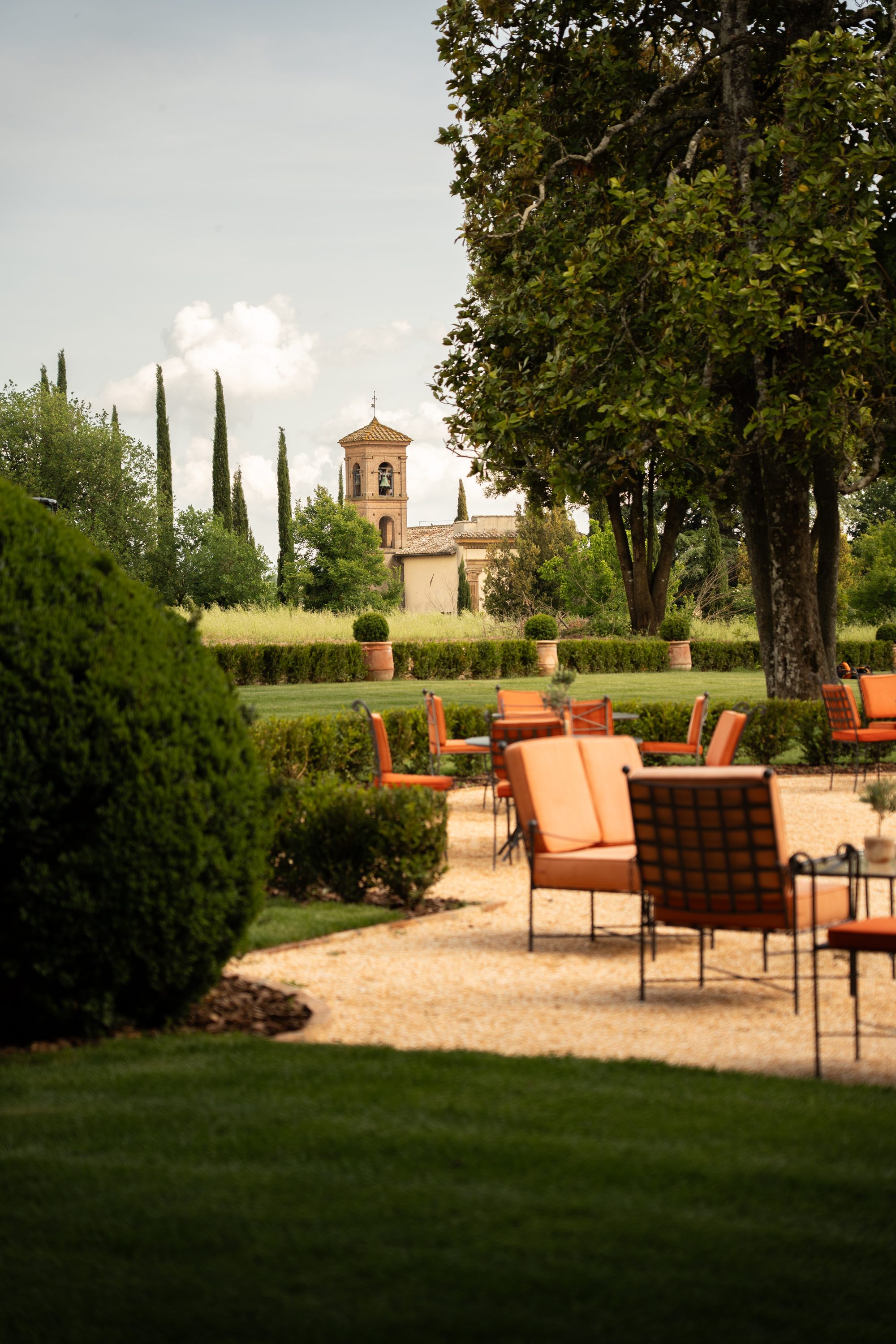 Il giardino di Volte Alte con le siepi tonde e i tavolini di metallo, e in fondo un campanile