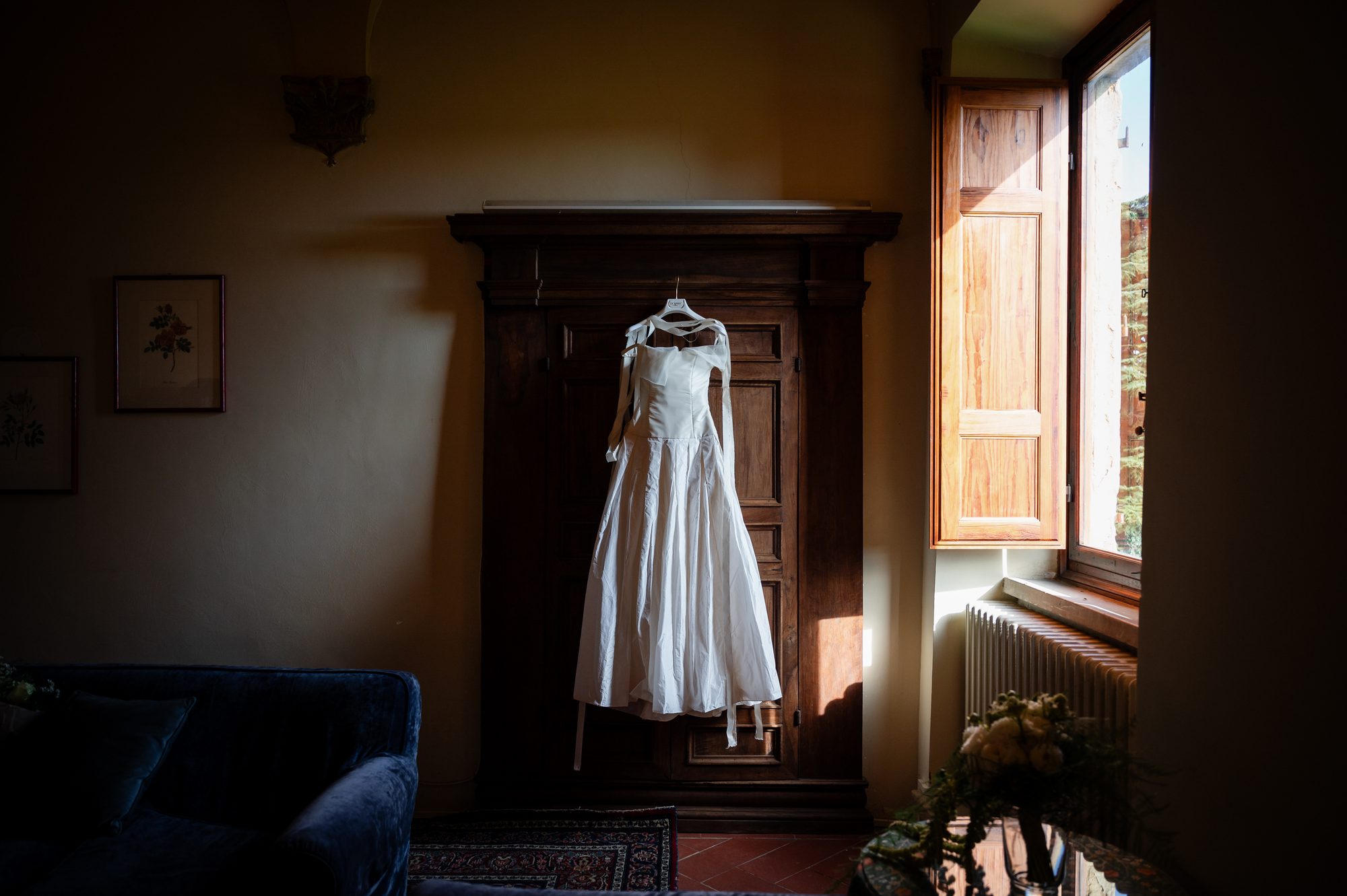 L'abito da sposa appeso a un armadio antico, con la finestra aperta sul verde